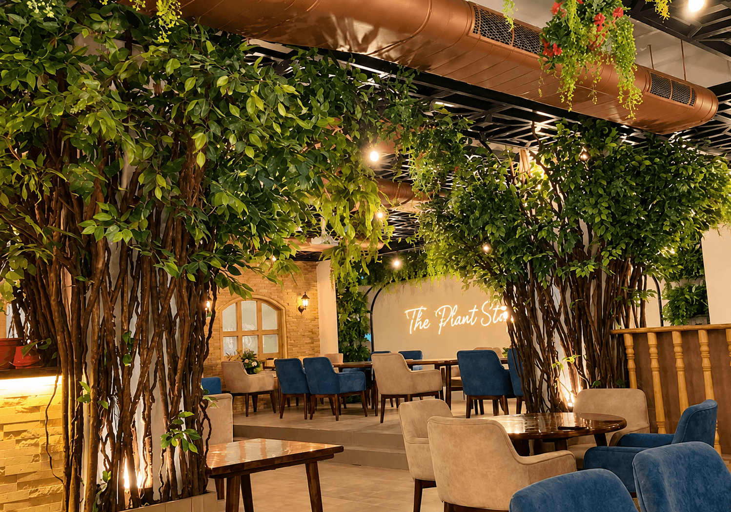 Indoor dining room at The Plant Story with tall indoor trees, hanging greenery and blue velvet chairs